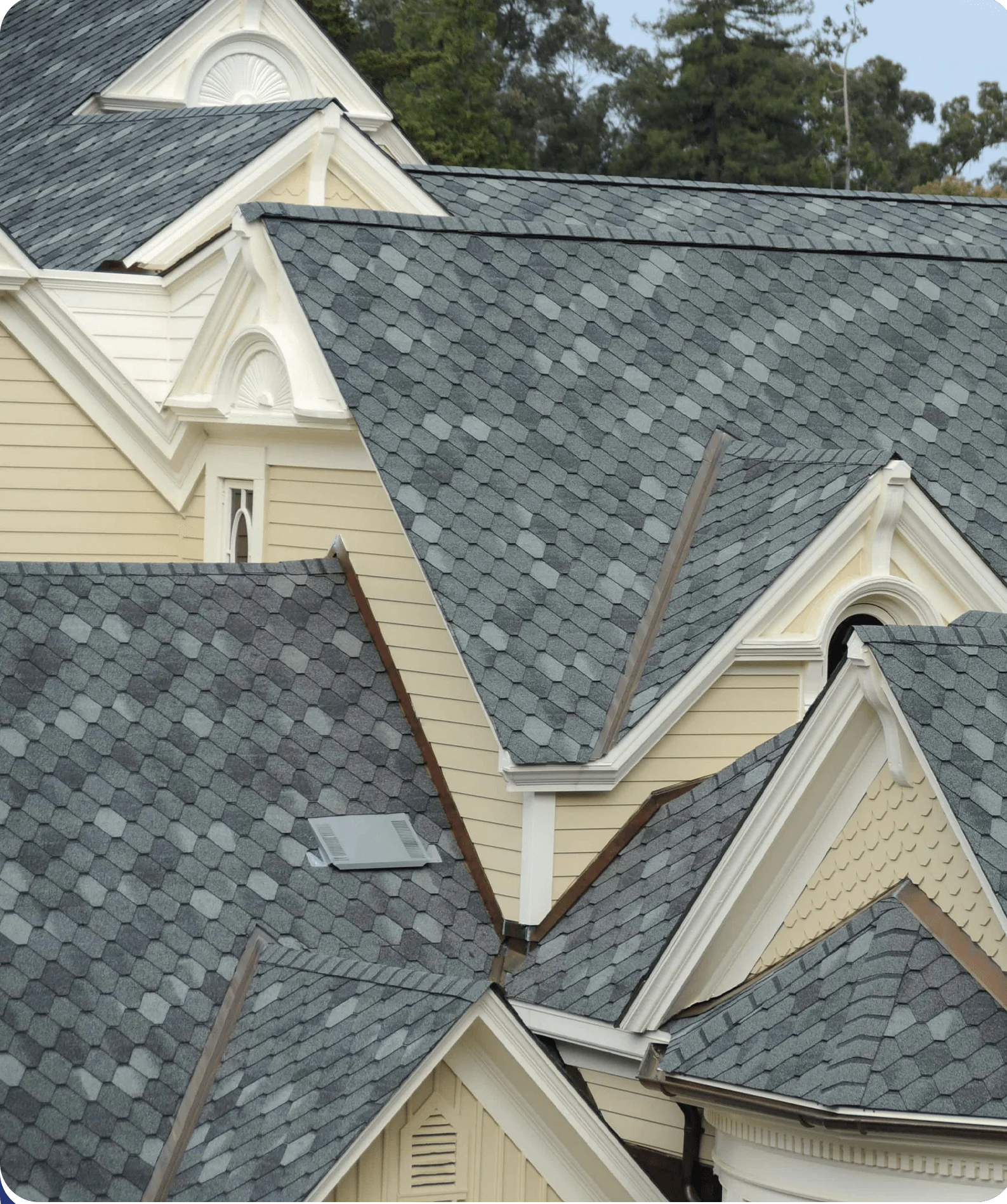 Multiple complex residential roof sections with distinctive gray cascade-style asphalt shingles and white architectural trim.